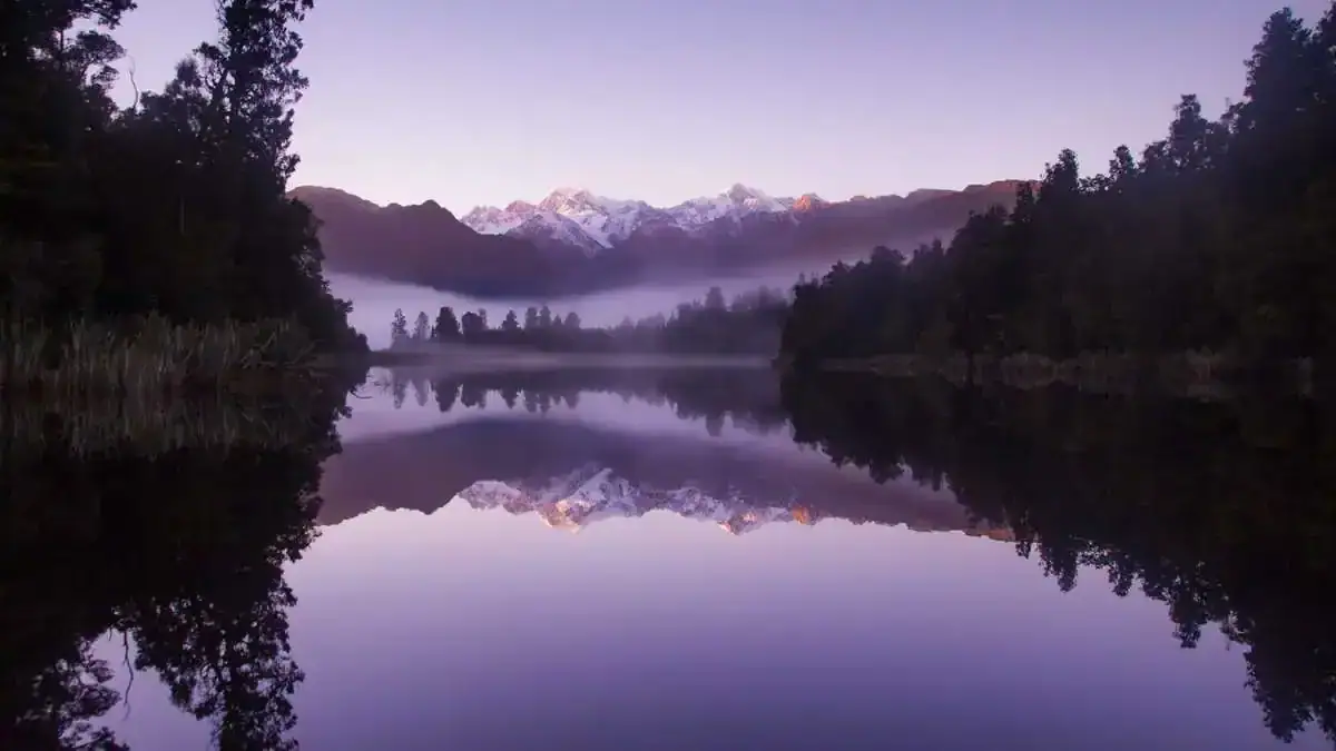 Calm mountain lake at sunrise with forest and snow peaks reflected in still water – symbolizing clarity and release for Overcome Feeling Stuck with EFT Tapping.